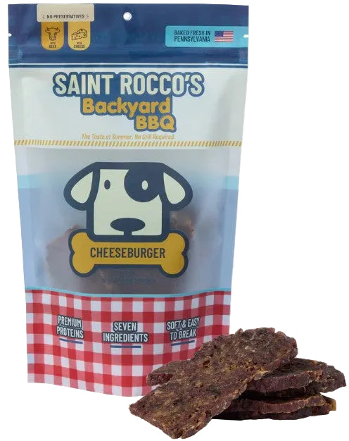 A package of Saint Rocco's Backyard BBQ Cheeseburger dog treats with several pieces of the dark brown jerky displayed in front on a white background.
